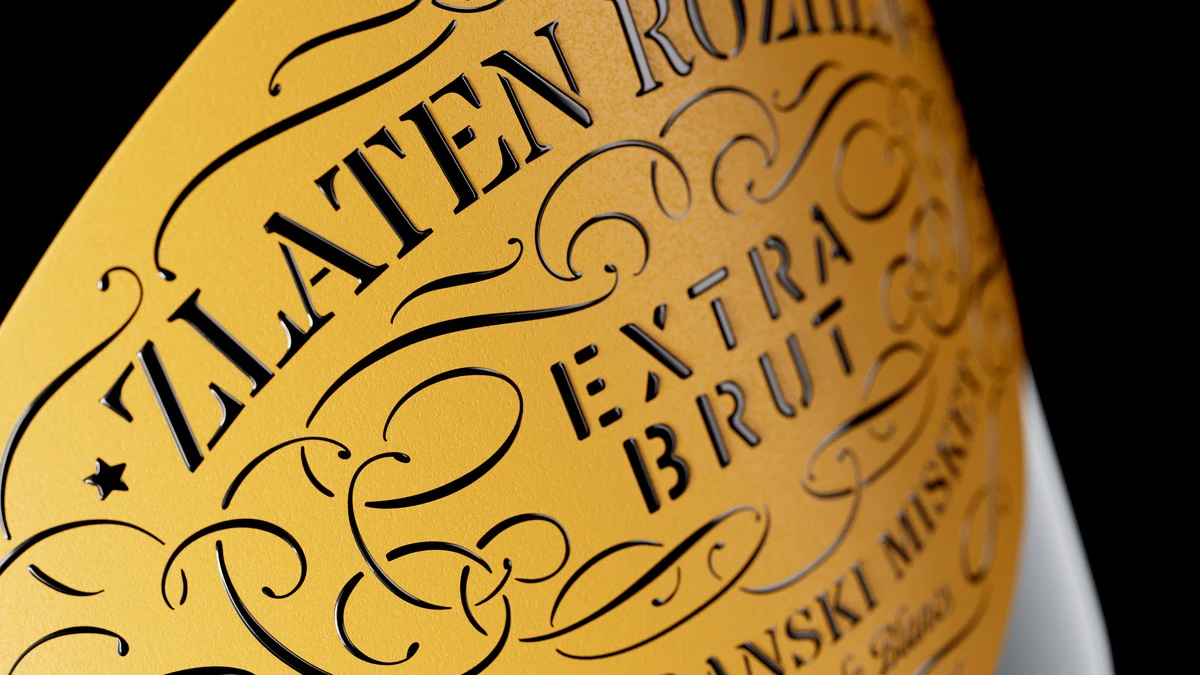 Diagonal macro of the hand-drawn ornaments and stencil lettering on the Zlaten Rozhen sparkling wine label, with relief varnish catching the light